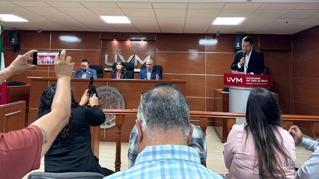 Front view of a university lecture hall: teachers and Interledger Foundation judges seated at a table, with one person addressing the students.