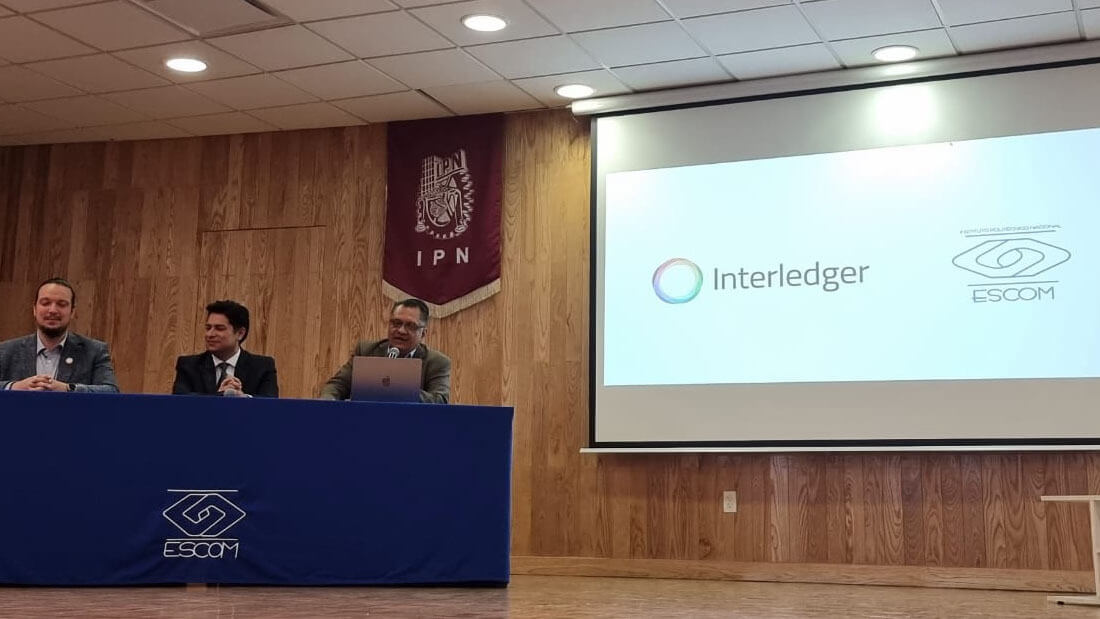 Front of a university lecture hall where teachers and ILF judges are seated at a table, with one person speaking to the students.